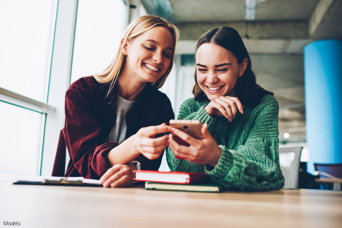 Two young women smiling while looking at a phone together